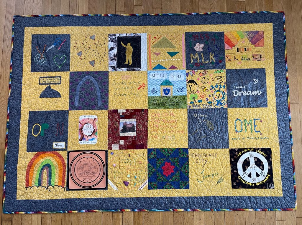 A quilt with dominant colors of gold and grey, six squares across and four rows down. 